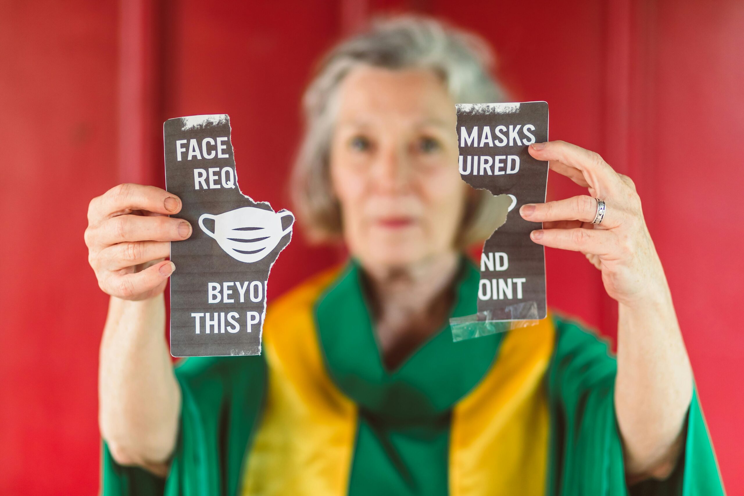 Senior woman holding torn COVID mask requirement sign symbolizing protest.